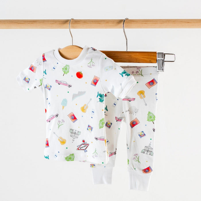 Children's organic sleepwear with colorful patterns on a wooden hanger against a white background