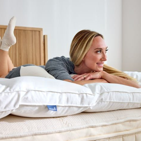 A woman lying on a bed with a white latex mattress topper, smiling.