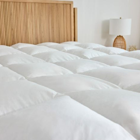 White box stitched latex mattress topper on a bed with a wooden headboard and lamp in the background.tched