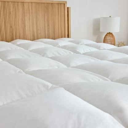 White box stitched latex mattress topper on a bed with a wooden headboard and lamp in the background.tched