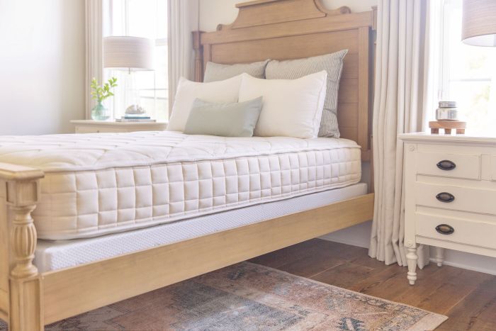 Bedroom with a wooden bed frame and Naturepedic Organic Chorus mattress, side table, and lamp.