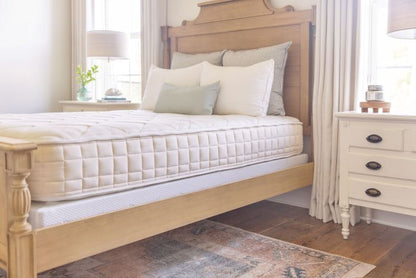 Bedroom with a wooden bed frame and Naturepedic Organic Chorus mattress, side table, and lamp.