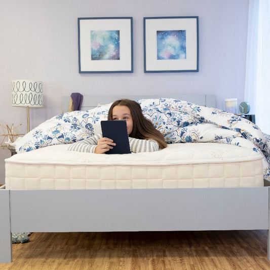 Girl reading on the bed on a Naturepedic Organic Verse Kids mattress  
