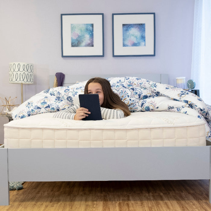 Girl reading on the bed on a Naturepedic Organic Verse Kids mattress  