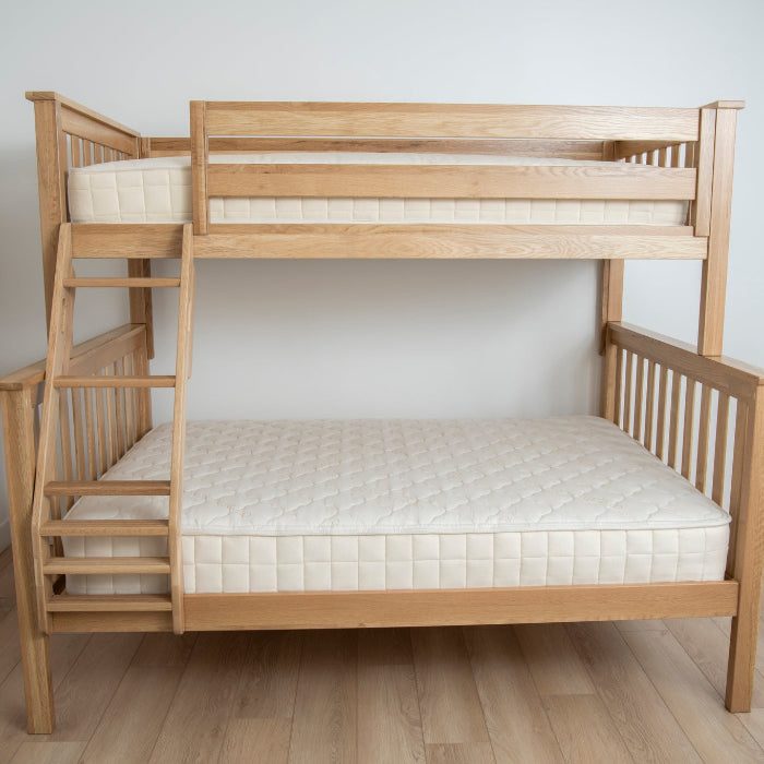 Wooden bunk bed with white mattresses on a wooden floor against a white wall.