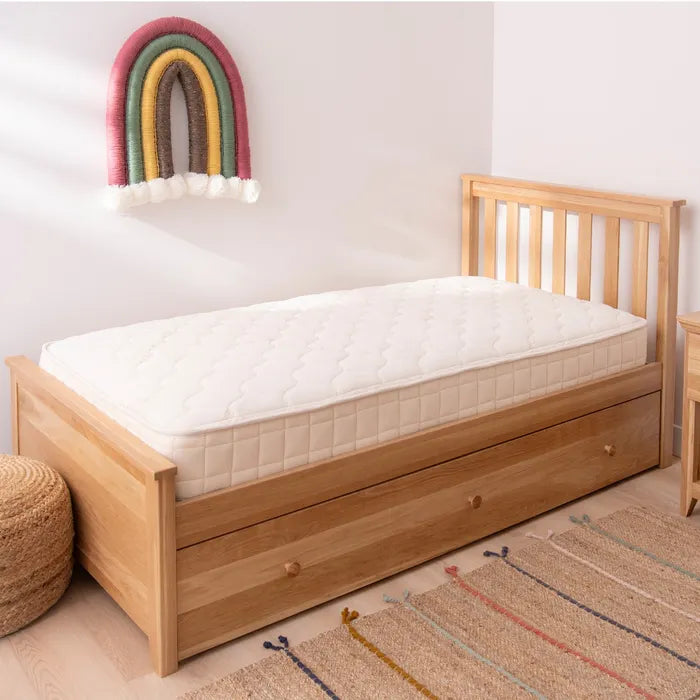 Wooden bed with white mattress in a room with a colorful rainbow decoration on the wall.