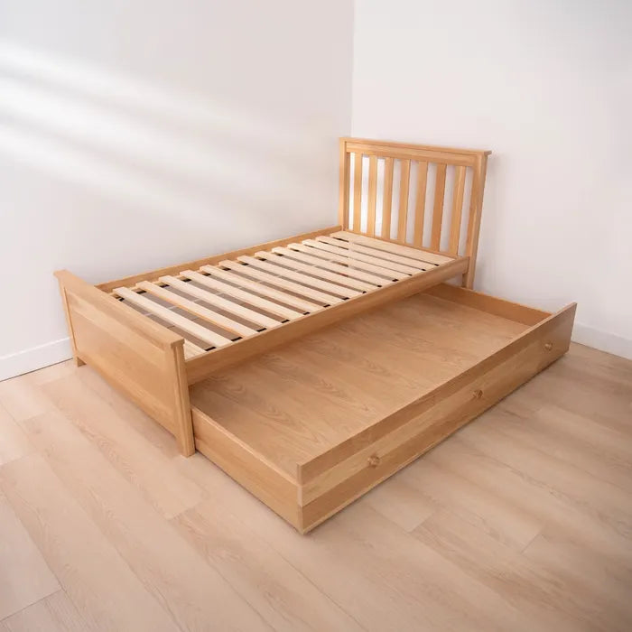 Wooden bed with pull-out drawer on a light wooden floor.