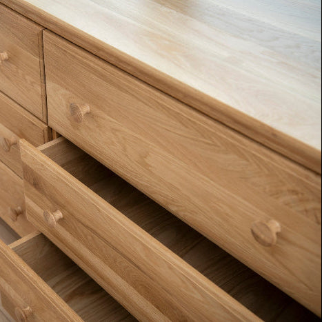 Wooden dresser with multiple drawers on a wooden floor.
