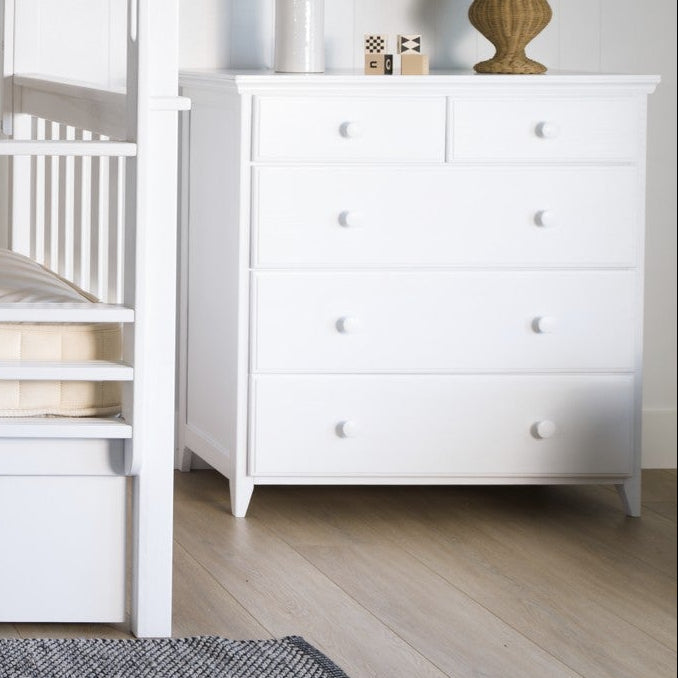White bunk bed in a room with a chest of drawers and decor items.