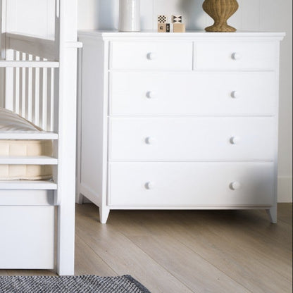 White bunk bed in a room with a chest of drawers and decor items.